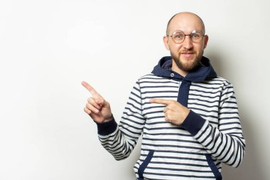 Kapüşonlu gözlüklü sakallı genç bir adamın portresi izole bir arka planda bir parmağı işaret ediyor. Duygusal bir yüz. Şok jesti, sürpriz.