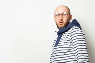 Gözlüklü kel bir genç adam portresi, kapüşonlu bir süveter, izole bir ışık arka planında korkmuş bir yüz. Duygusal bir yüz. Korkunun işareti, sürpriz.