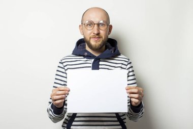 Gözlüklü kel bir genç adamın portresi. Kapüşonlu bir süveter. Önünde boş bir kağıt tutuyordu. Duygusal bir yüz. Boşluğu kopyala.