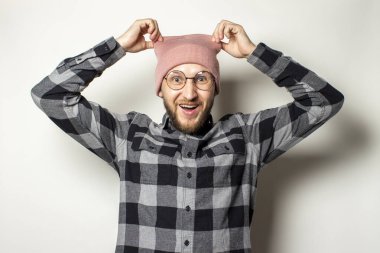 Şapkalı sakallı genç bir adamın portresi, ekose gömlekli, izole bir arka planda şapkasını çıkarıyor. Duygusal yüz..