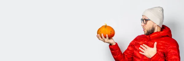赤いジャケットの若者に衝撃を与えた帽子はカボチャを持っていて胸に手を軽く背景に置いている ハロウィン お祝い 秋の概念 バナー — ストック写真