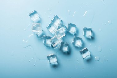 Mavi zemin üzerinde su olan buz küpleri. İçkiler için buz konsepti. Pankart. Düz yatış, üst görünüm.