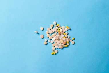 Mavi arka planda bir sürü farklı tipte hap var. Uykusuzluk, rejime göre haplar, vitaminler. Düz yatış, üst görünüm.