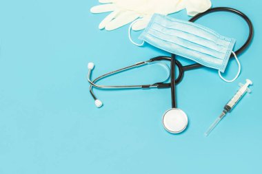 Tıbbi steteskop, lateks eldivenler, şırınga ve mavi arka planda koruyucu maske. İlaç, hemşire, hastane, güvenlik, salgın hastalık. Pankart. Düz yatış, üst görünüm.