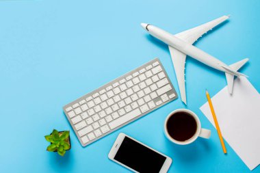 Klavye, çiçek, uçak, çay ya da kahve bardağı, boş bir çarşaf ve mavi arka planda bir kalem. Seyahat planlama, internetten uçak bileti alma, uçak bileti satma. Pankart. Düz yatış, üst görünüm.