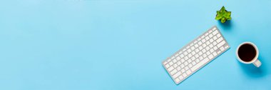 Klavye, çiçek ve fincanda çay ya da kahve mavi arka planda. Çalışma alanı kavramı, bilgisayarda çalışmak, serbest çalışmak, ofis. Pankart. Düz yatış, üst görünüm.