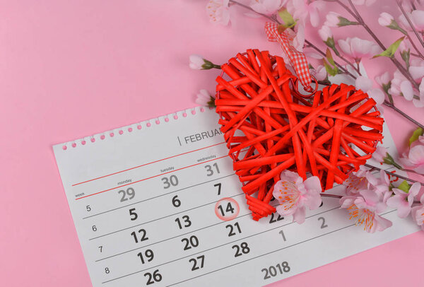 beautiful wicker red heart with pink flowers on a pink background background for a valentines day holiday with a calendar on February 14
