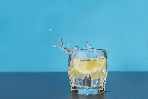 clear water drink in a glass splash splashing out of a glass with lemon citrus drops and splashes on a bare background