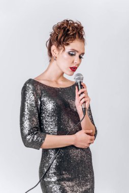 Mikrofonlu güzel bir genç kız beyaz bir arka planda şarkı söylüyor.