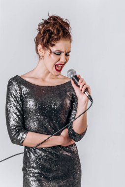 Mikrofonlu güzel bir kız soyutlanmış beyaz bir arka planda şarkı söylüyor.