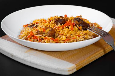 Doğu mutfağı kavramı. Siyah arka planda beyaz tabakta kuzu eti olan Özbek pilavı. Geleneksel Doğu yemekleri.