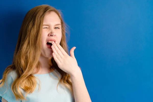 Menina em um fundo azul bocejos — Fotografia de Stock