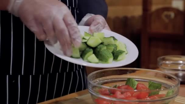 Man cooking cucumber salad with tomatoes in the kitchen with gloves — Stock Video