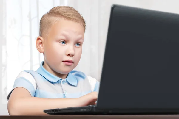 Vista lateral de um lindo menino europeu com olhos azuis sentado em um laptop de surpresa levantando as sobrancelhas olhando para a tela. Conteúdo proibido na Internet, conceito on-line de segurança infantil — Fotografia de Stock