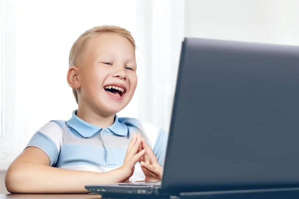 Bonito menino europeu bonito jovem ri alegremente e provocativamente enquanto sentado na frente de uma tela do laptop e assistindo a um vídeo engraçado, filme ou desenho animado. O conceito de um lazer feliz, divertido ou rela — Fotografia de Stock