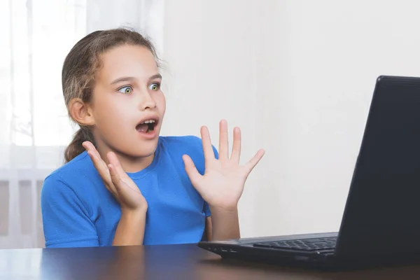 Uma linda garota adolescente bonita em uma camiseta azul em horror se afastou do laptop com os olhos e a boca bem abertos quando viu conteúdo proibido na Internet. Conceito Online de Segurança Infantil . — Fotografia de Stock