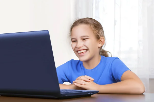 Piękny cute little girl siedzi przy komputerze i zabawy śmiejąc się patrząc na monitor laptopa. Uczenie się na odległość, rozmowy z przyjaciółmi w Internecie, rozrywka lub przeglądanie stron internetowych — Zdjęcie stockowe