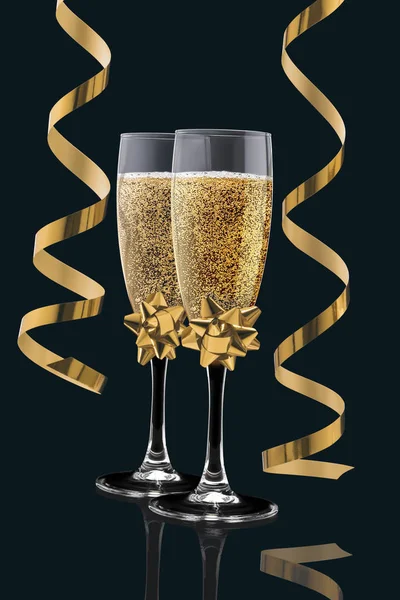 Deux élégants verres parfaits remplis de champagne pétillant avec deux banderoles dorées de serpentine isolées sur un fond noir. Noël, Nouvel An, anniversaire, concept de célébration — Photo