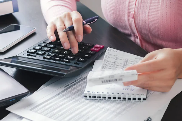 La contadora de la oficina tiene un cheque de caja en sus manos y hace cálculos en una calculadora, anotando los resultados en un cuaderno. El concepto de cálculo de impuestos, gastos, beneficios —  Fotos de Stock