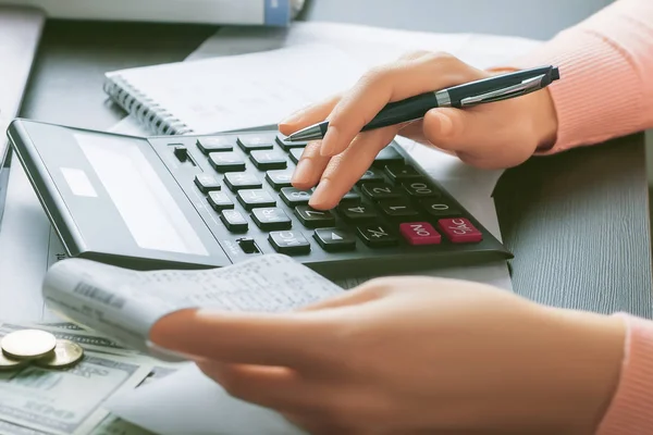 Kadın bir muhasebeci elinde bir kasiyer tutuyor ve hesap makinesiyle hesaplamalar yapıyor. Kâr analizi, vergilerin hesaplanması, harcamalar ve ödemeler, ofis işi kavramı