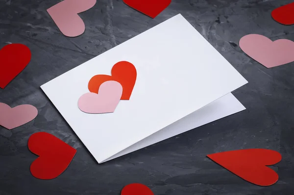 空白情人节贺卡的侧面视图，卡片上装饰着两只手工制作的心和分散在纸上的各种形状的心，背景为黑色，有复制空间 — 图库照片