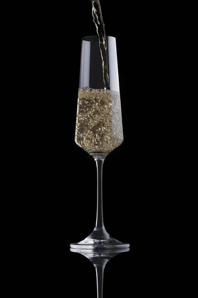 Golden champagne giet in een transparante luxe elegant glas geïsoleerd op zwarte achtergrond. Mousserende wijn met bubbels vult het glas — Stockfoto