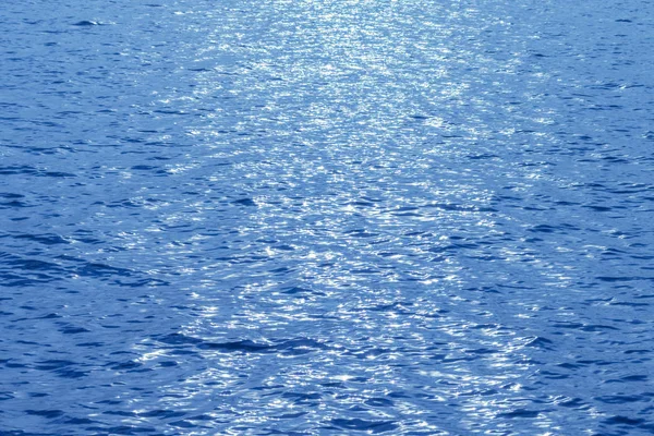 Vista lateral del mar azul con el resplandor del sol poniente en el centro en la superficie del agua. Fondo abstracto de textura de agua azul — Foto de Stock