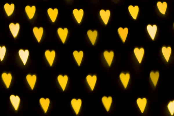 Verschwommene gelbe Lichter in Herzform. defokussierte Straßendekorationen und Girlanden. Valentinstag, Liebe, abstrakte trendige Textur Hintergrund — Stockfoto