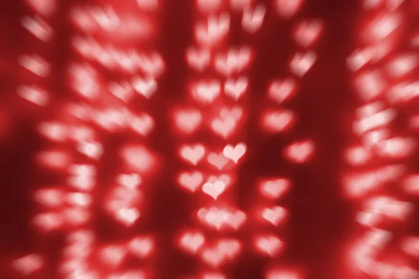 Rozmazaná červená světla ve tvaru srdce. Rozostřené pouliční dekorace a věnce. Valentýn, láska, abstraktní módní textura pozadí — Stock fotografie
