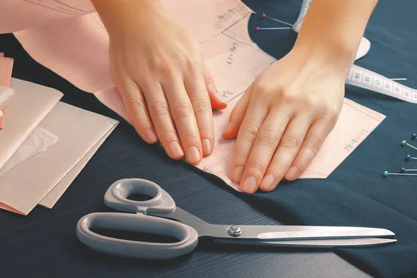 Close-up van de handen van een jonge naaister meisje die een van de patronen bevestigd aan de rand van de stof met behulp van een naaipin. — Stockfoto