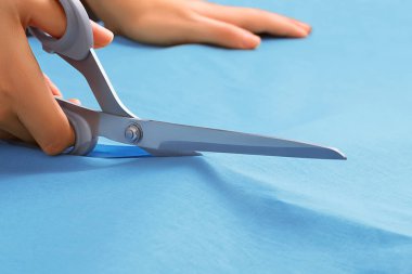 Close up side view of sewing scissors in the hands of a girl cutting blue fabric clipart