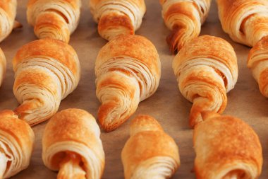 Üç sıra taze pişmiş altın kruvasanın yan görüntüsü kabarık hamur işlerinden yapılmış sığ bir tarla derinliği ve kahverengi kabartma kağıdında reçel var.