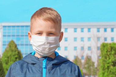 Dışarıdaki hastanenin arka planında koruyucu bir maske takan üzgün Avrupalı çocuk. Viral enfeksiyon önleme, virüs koruma kavramı