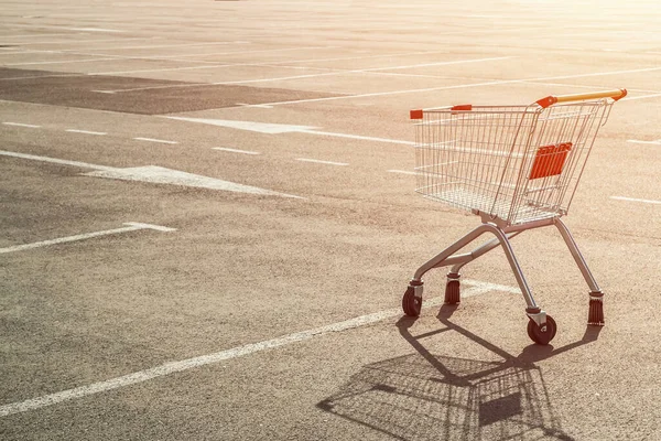 Empty single grocery cart in an empty parking lot near a supermarket at sunset. Panic during a pandemic, goods sold out, out of stock concept.