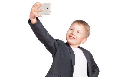 Sevimli, çekici, gülümseyen çocuk, uzanmış kolunda bir telefon tutuyor ve kendi fotoğrafını çekiyor. Selfie çeken çocuk izole edilmiş beyaz arka plan.