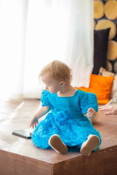 Uma criança em um vestido azul senta-se à janela — Fotografia de Stock