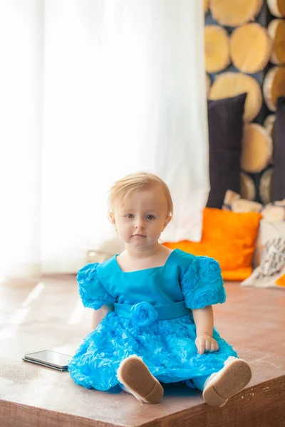 Ένα παιδί με μπλε φόρεμα κάθεται στο παράθυρο. — Φωτογραφία Αρχείου