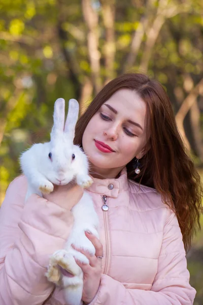 Menina atraente em um casaco rosa com um coelho branco-neve. conto de fadas — Fotografia de Stock
