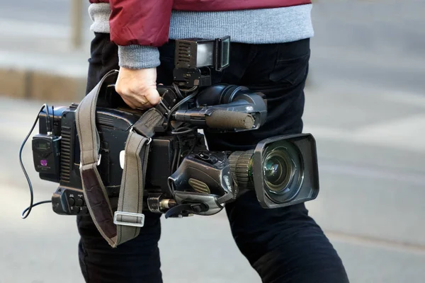 cameraman holding his professional camcorder in the street. Operator in social environment, filming, news outlet, motion-picture cameraman