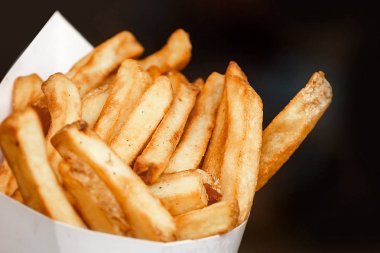 Kağıt pakette bulunan patates kızartması. Sokak gıda. Koyu arka plan. Metin ve boşaltmak için yer. Yatay görünüm.