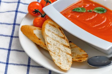 Fesleğen, tost ve domates ile beyaz bir tabak içinde domates çorbası. 