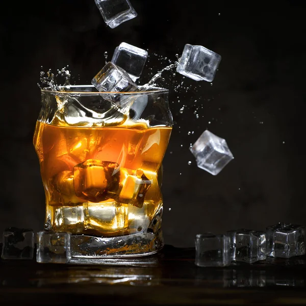 Jégkocka öntsük egy pohár alkohol. Fröccsenő, sötét háttér előtt. Hely, a szöveg másolása. — Stock Fotó