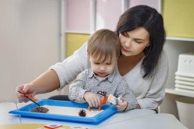 Bebek bakıcısı ile küçük bir çocuk oynar. Kuma çizer. Çocuk anne kucağına oturur. Çocukluk ve ebeveynlik kavramı. El ele. Yetimhane ve evlat edinme kavramı