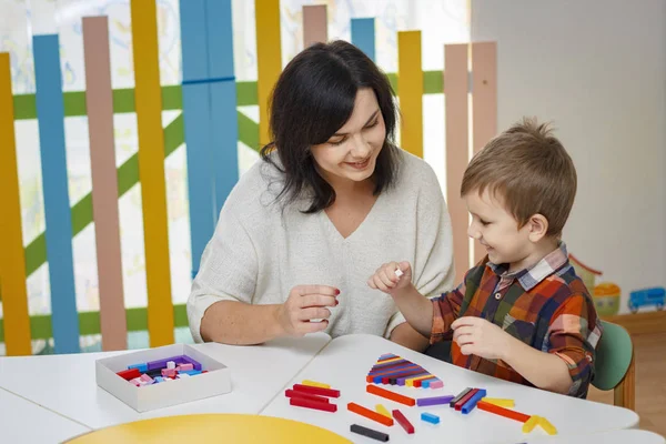 Mamă, profesoară, dădacă învaţă copilul. Pe masă sunt obiecte colorate. Învățarea conceptului în grădiniță . — Fotografie, imagine de stoc