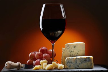 Bardak şarap üzüm ve bir parça peynir kalıp, Parmesan peyniri ve peynir bıçağı. Turuncu arka plan.