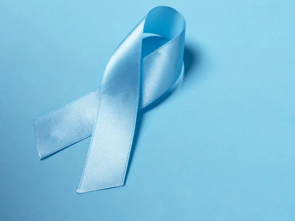 Closeup a Blue satin Ribbon symbol of prostate cancer awareness on a bright blue background. Concept of medicine and health care — Stock Photo, Image