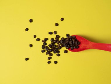 kavrulmuş kahve çekirdekleri kırmızı plastik bir kaşıktan sarı bir kağıda dökülüyor.