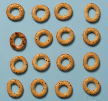 Ekmek simitleri mavi arka planda serili. Diğerlerinin arasında göze çarpan biri var. Üst görünüm.