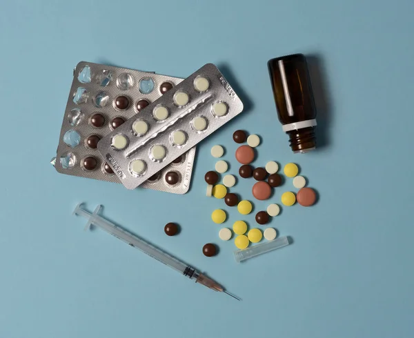 Шприц і різні ліки, ліки, пігулки і вітаміни викладені на синьому тлі. Здоров'я та аптека, вигляд зверху, площадка — стокове фото