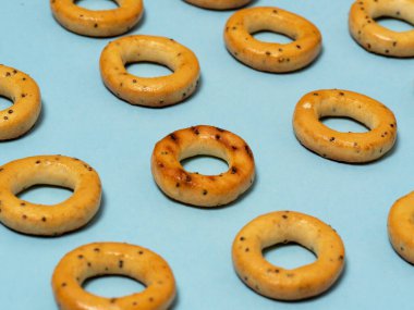 Ekmek simitleri mavi arka planda serili. Diğerlerinin arasında göze çarpan biri var..